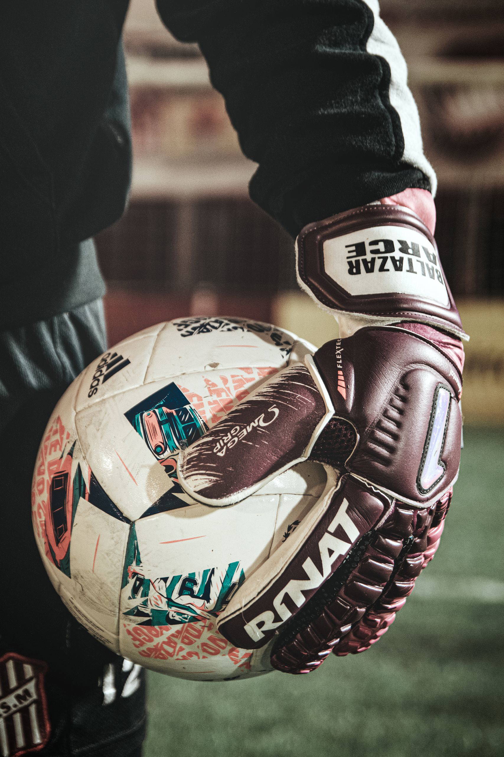Focused shot of soccer goalie wearing gloves holding a ball on the field.