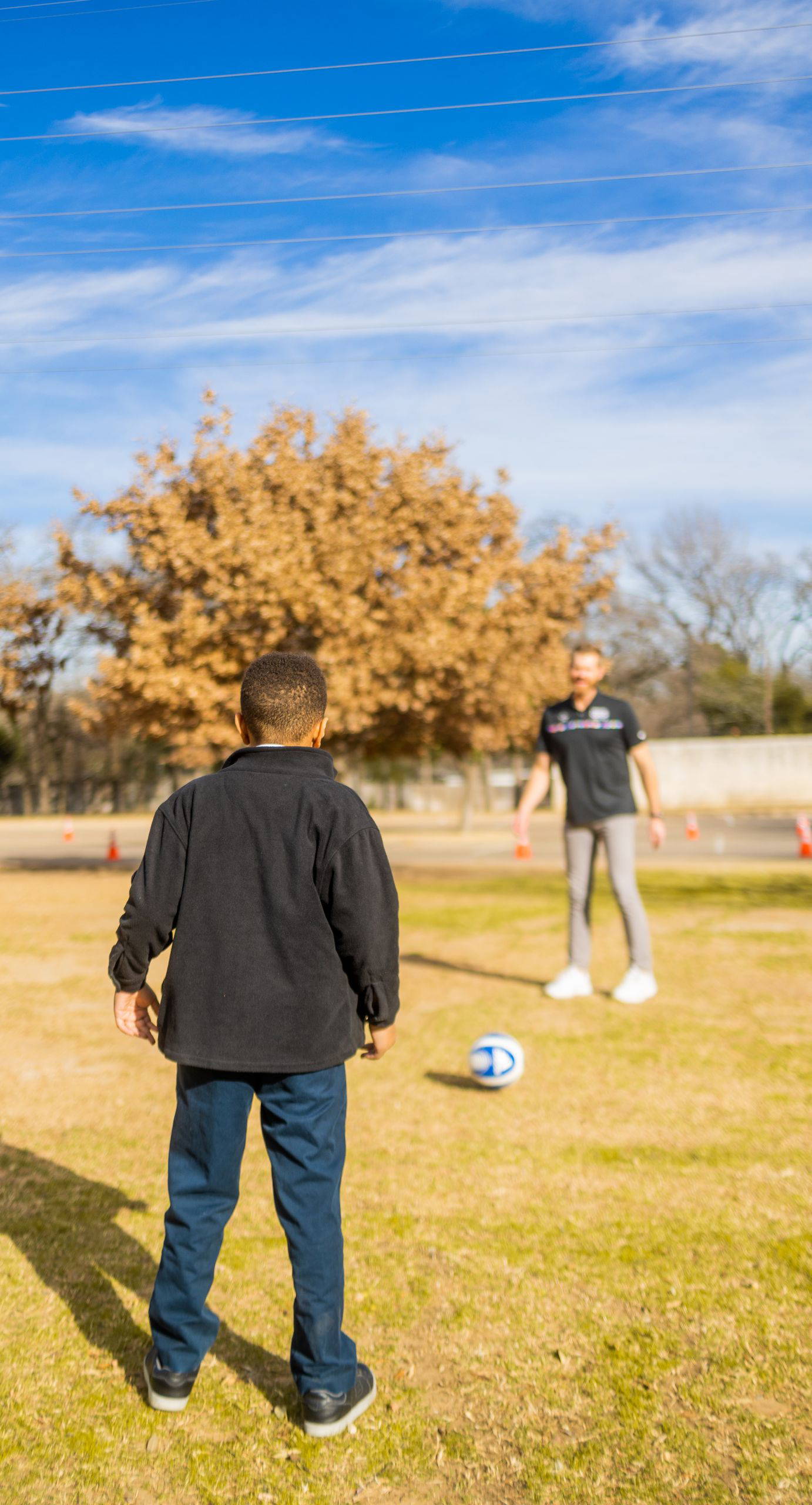 Young boy playing soccer with a coach during a sunny outdoor session. Perfect for sports and youth training themes.